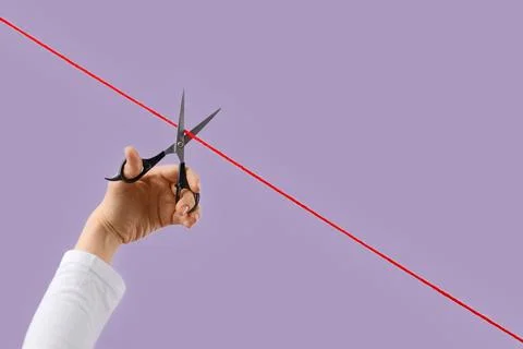 Hand cutting red thread with scissors on purple background Stock Photos