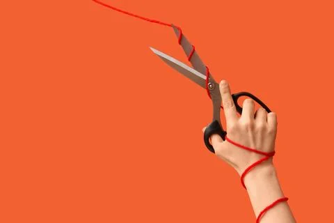 Hand cutting red yarn with scissors on orange background Stock Photos