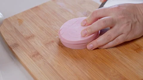 Hand cutting a stack of pink bologna sausage slices with a knife on a woode.. Stock Footage 347182411
