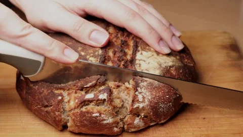 Hand cutting through fresh rustic homemade bread loaf with serrated knife on Stock Footage 311511318