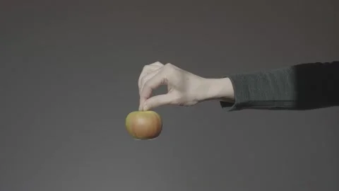 A hand on a dark background holds out a green apple holding it by the stalk. App Stock Footage 233001226