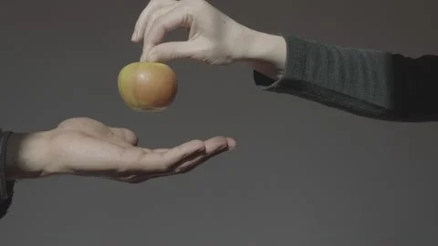 A hand on a dark background holds out a green apple holding it by the stalk. The Stock Footage 233001241