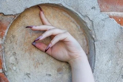 Hand with dark nails rests in circular stone opening Stock Photos