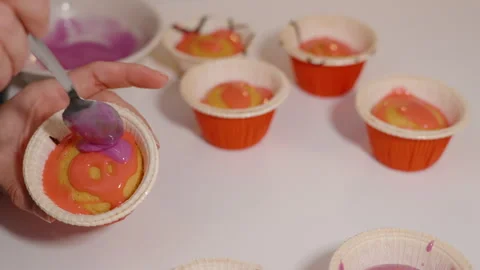 Hand Decorating Cupcake with Purple Icing Over Pink Glaze Held in Red Wrapper as Stock Footage 308210058