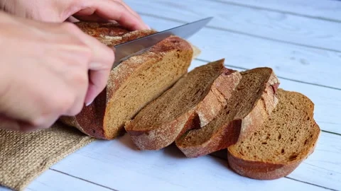 Hand delicately slices through crispy bread with knife on wooden board. Perfect Stock Footage 267988789
