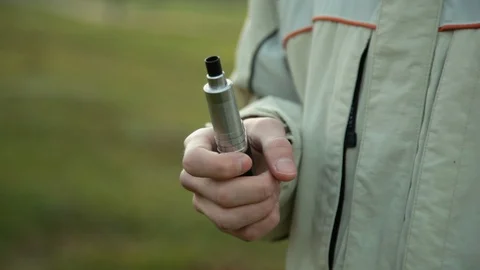 Hand with device of vaping young man in the park in the evening Stock Footage 121061715