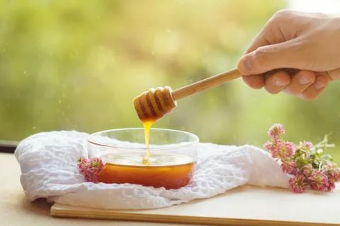 Hand with dipper collecting honey from a cup of honey. Glass bowl of honey Stock Photos