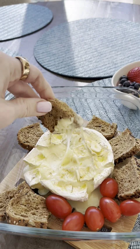 Hand dipping bread into baked camembert with honey drizzle and tomato Stock Footage 318553287