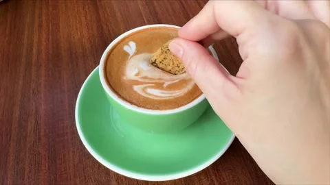 Hand dipping a cookie into a cup of hot cappuccino with latte art 스톡 동영상 335018047