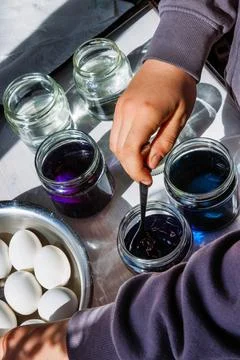 Hand dipping egg into the blue dye glass jar for easter egg coloring in sun.. Stock Photos