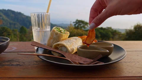 Hand Dipping Fried Snack Into Sauce On Plate With Wraps And Drink On Wooden Tabl Video stock 334320292