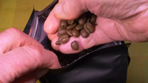 A hand dipping into a pack of coffee beans, then lifting some out to look at. Stock Footage 291873601