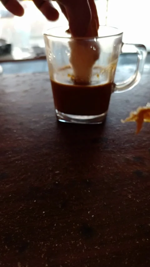 Hand dipping a piece of bread into a glass cup of coffee on a wooden table. Stock Footage 333120703