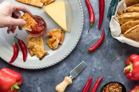 A hand dipping a piece of crisp cracker bread into a jar of hot pepper jelly. Stock Photos