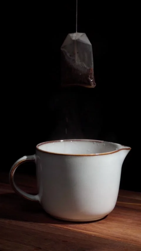 Hand dipping tea bag into hot cup with steam dark background vertical Stock Footage 324760935