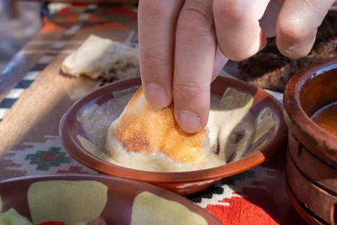 Hand dipping toasted bread into hummus in a clay bowl on a colorful tableclot 스톡 사진