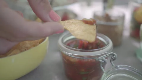 Hand Dipping a Tortilla Chip in Salsa at a Bright Outdoor Picnic Setup Stock Footage 293237572