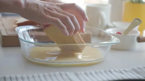 Hand dips bread in egg mixture in glass dish on kitchen counter Stock Footage 339632656