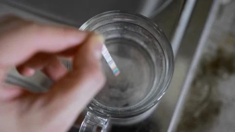 Hand dips DIY test strip into clear glass of tap water for quality analysis at Stock Footage 329214085
