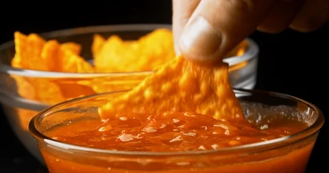 Hand dips tortilla chip into salsa sauce on black background close-up Stock Footage 122079023