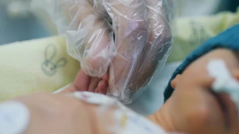 A hand in disposable glove is stroking baby's hand Video stock 119692292