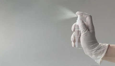 Hand in disposable gloves using Alcohol spray on gray background with copy sp Foto stock