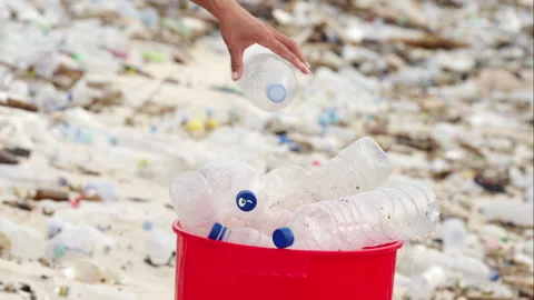 Hand disposing of a plastic bottle into a recycling bin amidst beach litter Stock Footage 271622577