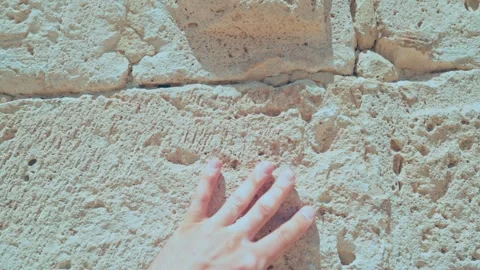 Hand with distinct vitiligo touching an ancient, weathered stone wall Stock Footage 346704981