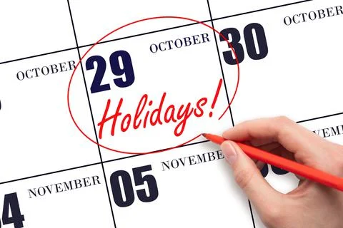Hand drawing a red circle and writing the text Holidays on the calendar date  Stock Photos