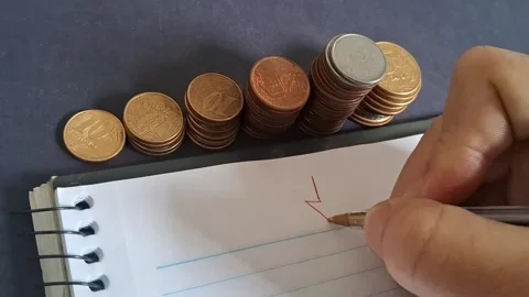 Hand drawing red downward arrow beside coin stacks Stock Footage 345448488