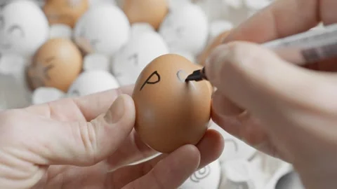 Hand drawing sad face on brown egg. Chicken eggs in container. Funny eggs. Video stock 304552392