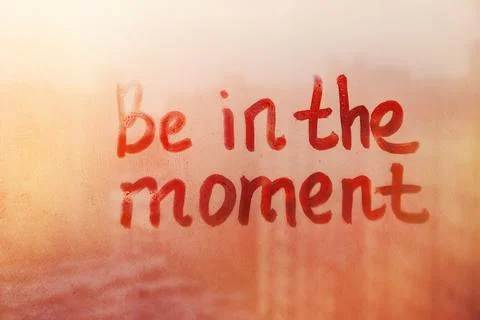 Hand drawn message Be in the moment on foggy glass on suset window Stock Photos