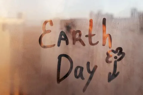 Hand drawn message Earth Day and flower shape on foggy glass of sunset window Stock Photos