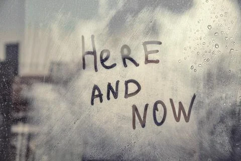 Hand drawn message Here and now on foggy glass on city window Stock Photos