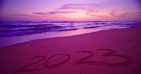 Hand-drawn numbers 2023 text in sand, Ocean sunrise or sunset light on the beach Stock Footage 250376616