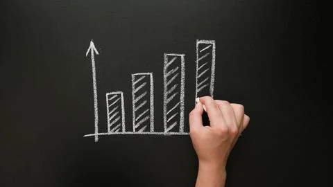 A hand draws a growing graph with chalk on a blackboard Stock Photos