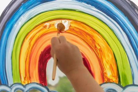 Hand draws a rainbow on the window. Rainbow on the glass. Close. Front view. Stock Photos