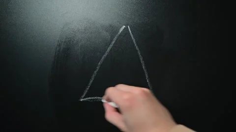 A hand draws a triangle shape using chalk on a dark surface in a well-lit area. Stock Footage 338186403
