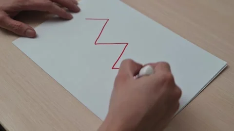 A hand draws zigzag lines on a plain piece of paper using a red marker. The Vidéo 337550130