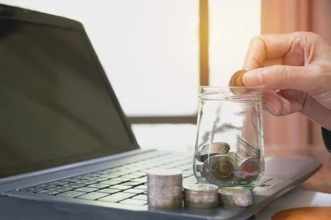 Hand drop the coin in jar with stack coins on laptop. Financial, accounting a Foto stock