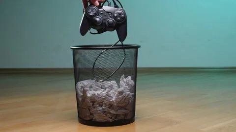 Hand dropping a black wired video game controller into a metal mesh trash bin Stock Footage 342771936