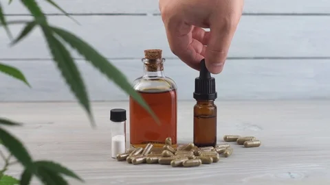 Hand dropping CBD oil from pipette to the bottle on White table with Marijuan Stock Footage 107072065