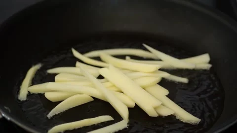 Hand dropping cut potatoes into hot oil for frying Stock Footage 329200185