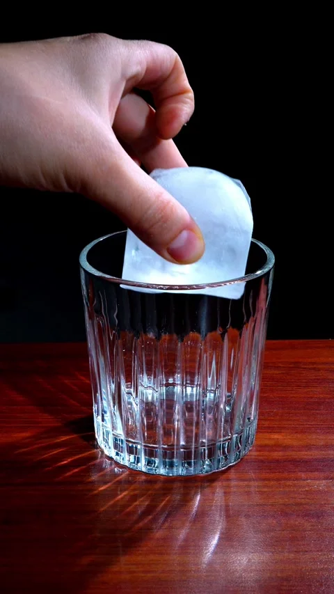 Hand Dropping Large Ice Cube into Crystal Glass Dark Background Vertical Stock Footage 324597507