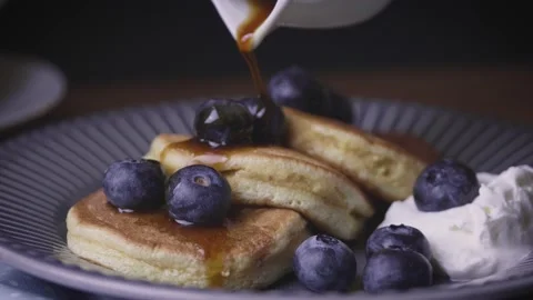 Hand dropping maple syrup on blueberry pancakes in a plate. Traditional food  Stock Footage 145580026