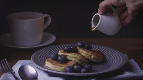 Hand dropping maple syrup on blueberry pancakes in a plate. Traditional food Stock Footage 145580027