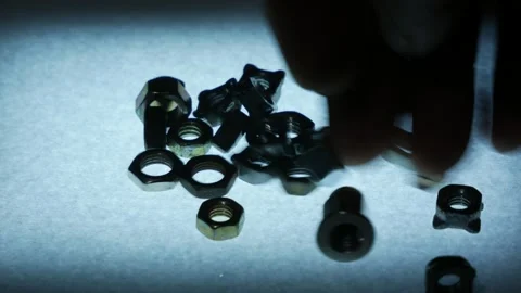 Hand Dropping Multiple Metal Hex Nuts onto Textured Surface Stock Footage 340069065
