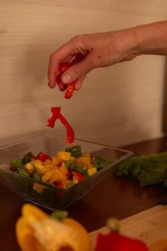A hand dropping red bell pepper slices into a glass bowl Stock Photos