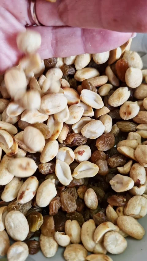 Hand Dropping Roasted Peanuts Into Bowl of Healthy Raisin Snack Mix Stock Footage 339001967