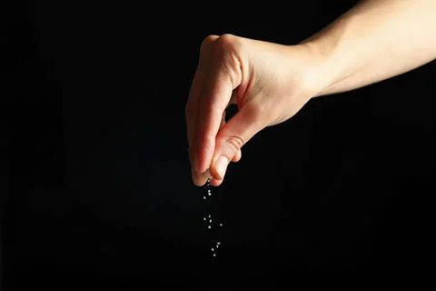 Hand dropping small white grains over dark background Fotos Stock